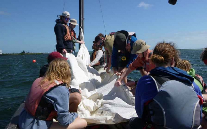 a group of people work on the fabric of a sail on a sailboat